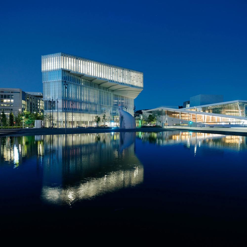 Foto av Deichmanske Bjørvika som speiles i vannet med Operaen på høyre side.