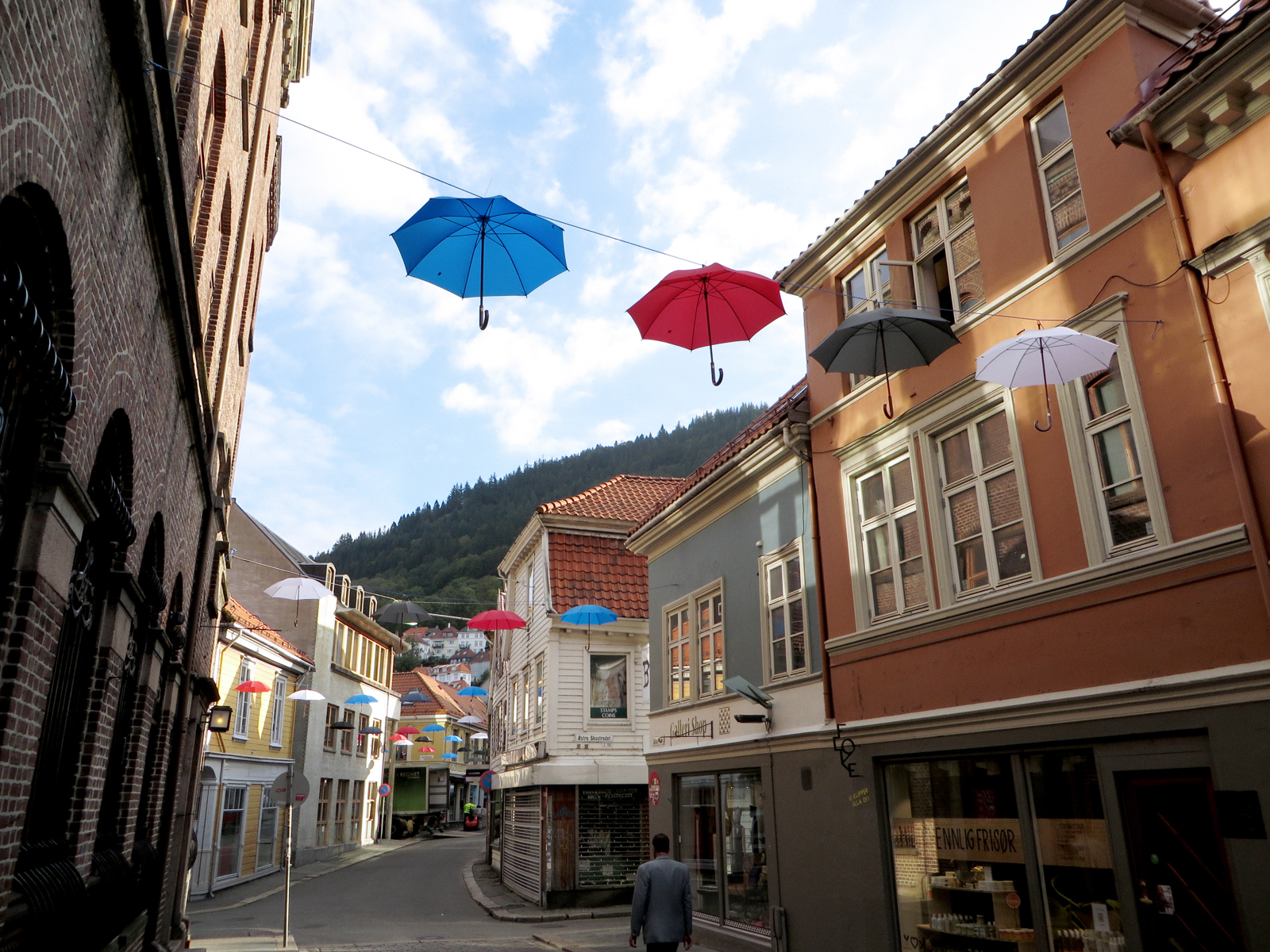 Foto av bygate med små varierende hus og paraplyer hengende over gata. 