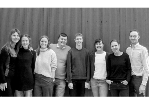 Foto av en gruppe voksne mennesker fremfor en vegg. Svart hvitt.