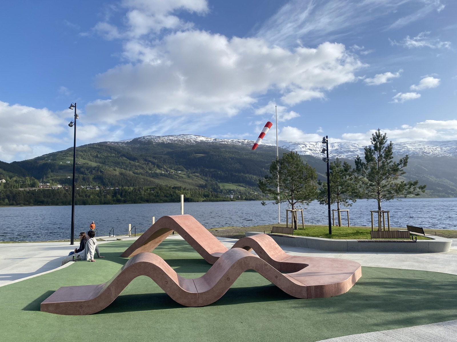 Foto av skulptur benk i en park, vann og fjell i bakgrunnen.