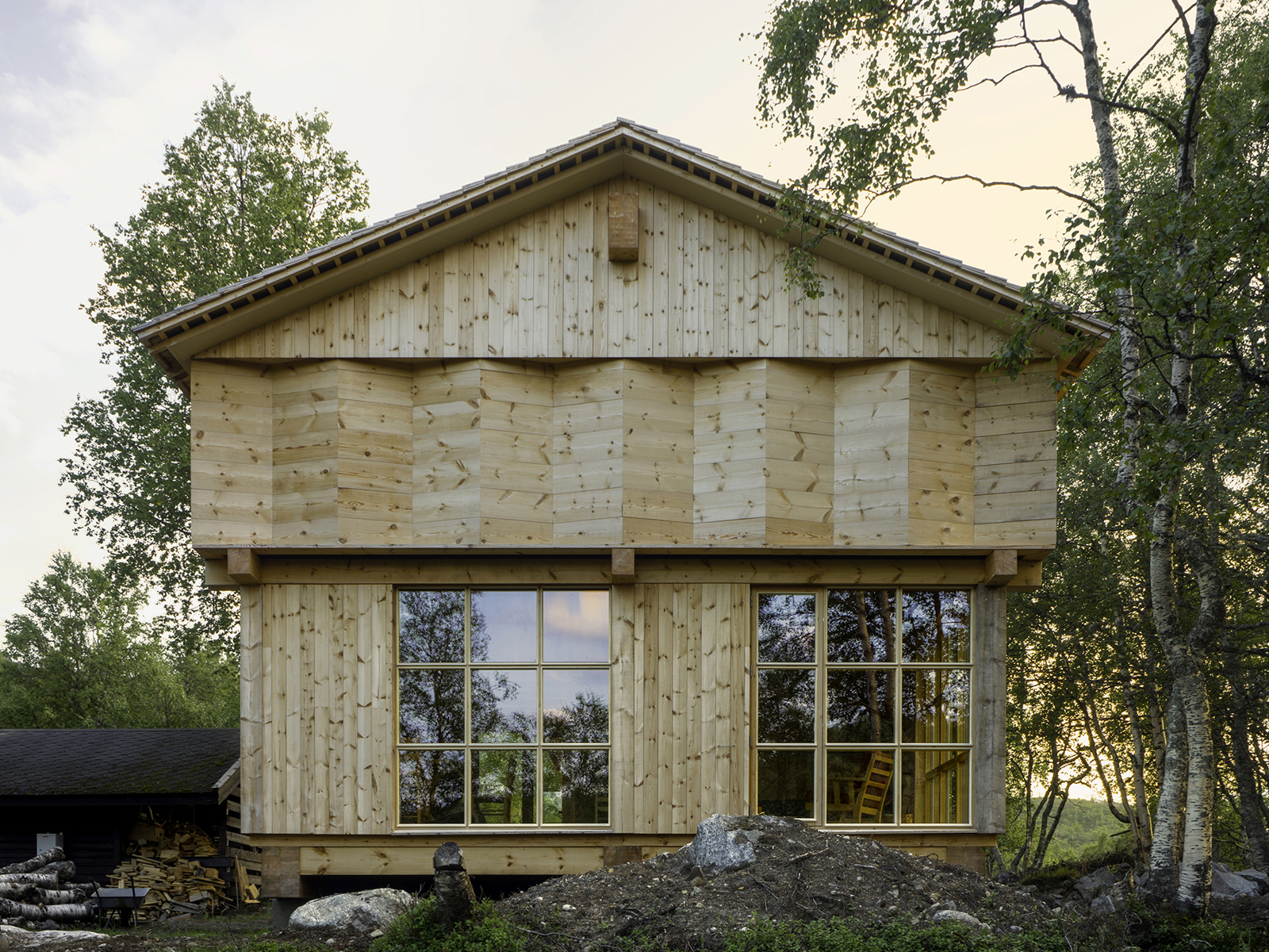 Hytte i treverk og med saltak inne i skogen. Foto.