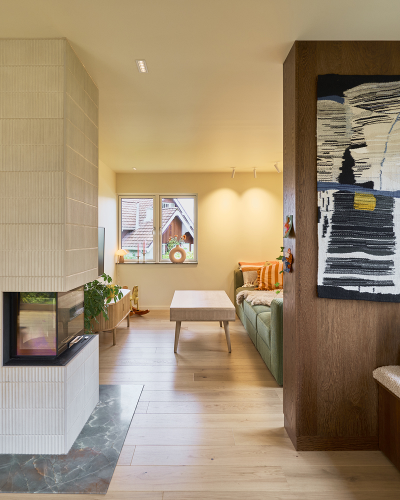 Interiørfoto av stue med peis kledd i fliser til venstre og sittebenk i tre til høyre