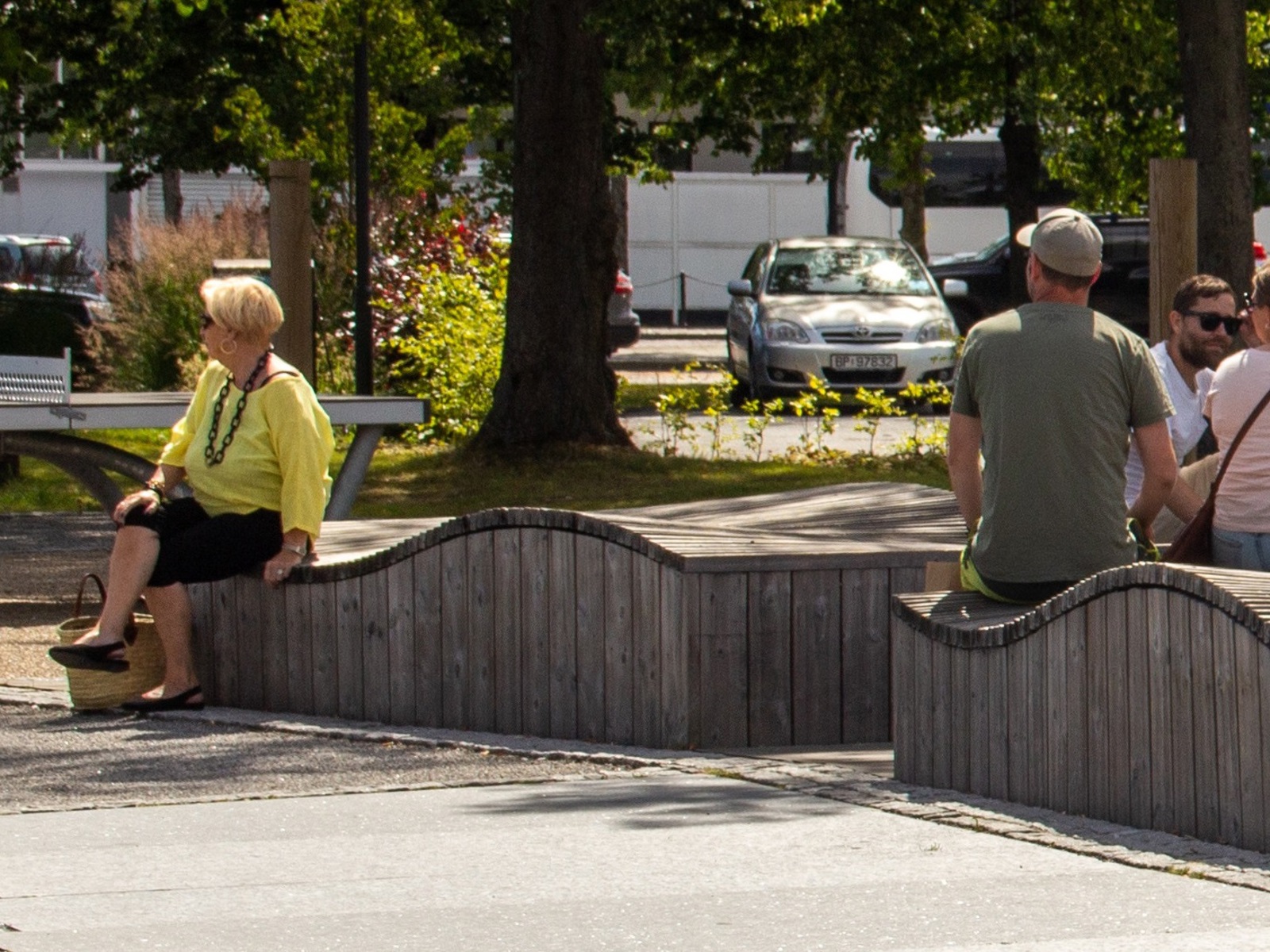 Foto av buet benk i parkområde med flere som sitter på den.