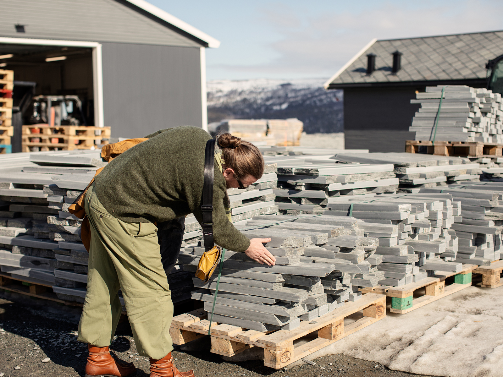 Foto av en mann som ser på skifer stablet på paller utendørs.