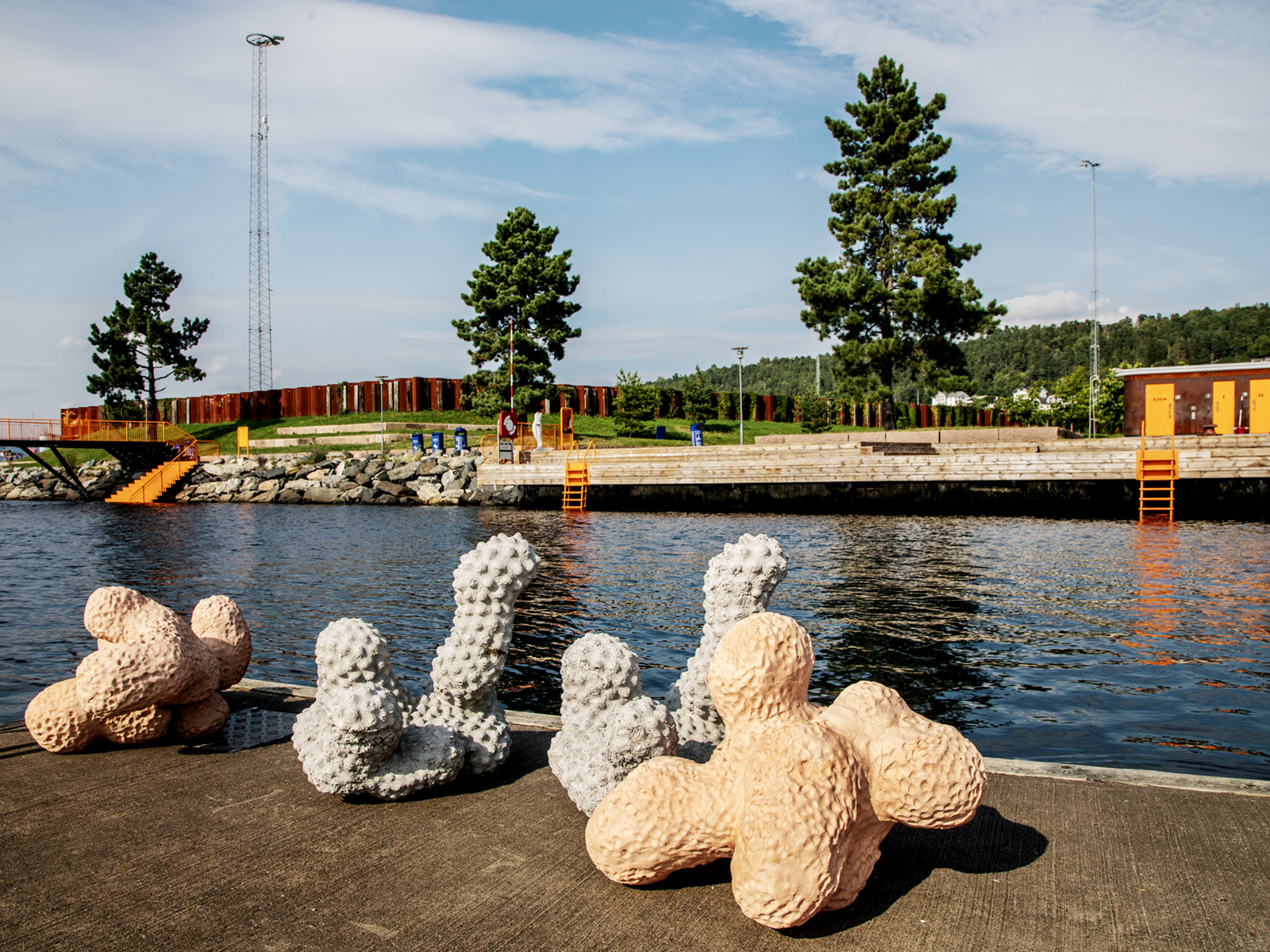 Foto av ulike figurer og former på bryggekant, badeanlegg i bakgrunnen.