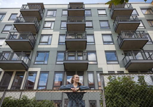 Foto av en dame som lener seg over gjerdet utenfor en boligblokk.