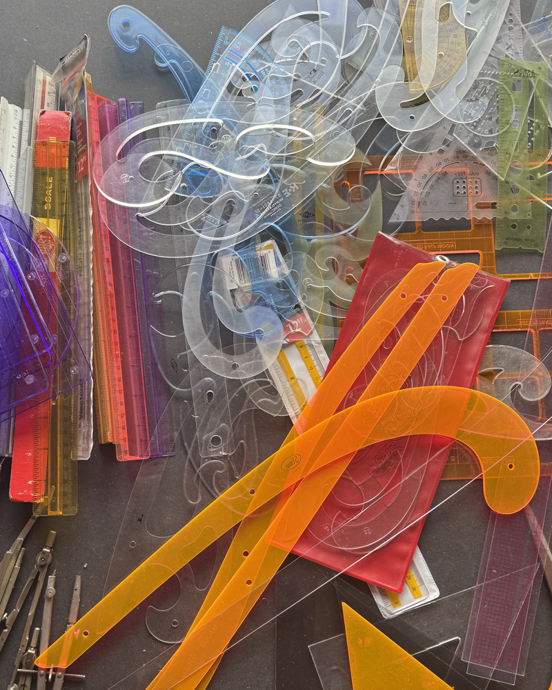 Foto av tegnesaker i en haug, mange ulike linjaler og passere osv.