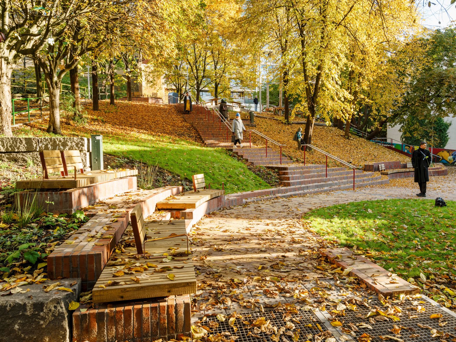 Foto av en park på en fin høst dag, benker, folk og trapp.