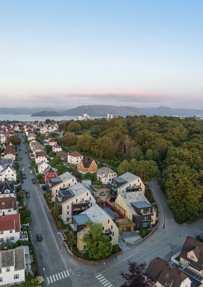Oversiktsfoto av by med småhus, hav, fjell og himmel i bakgrunnen.