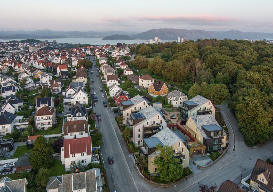 Oversiktsfoto av by med småhus, hav, fjell og himmel i bakgrunnen.
