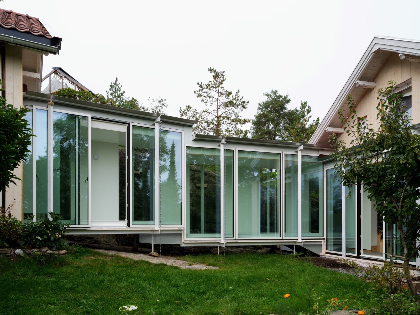 Eksteriør foto av moderne mellombygg i glass mellom to enebolig trehus.