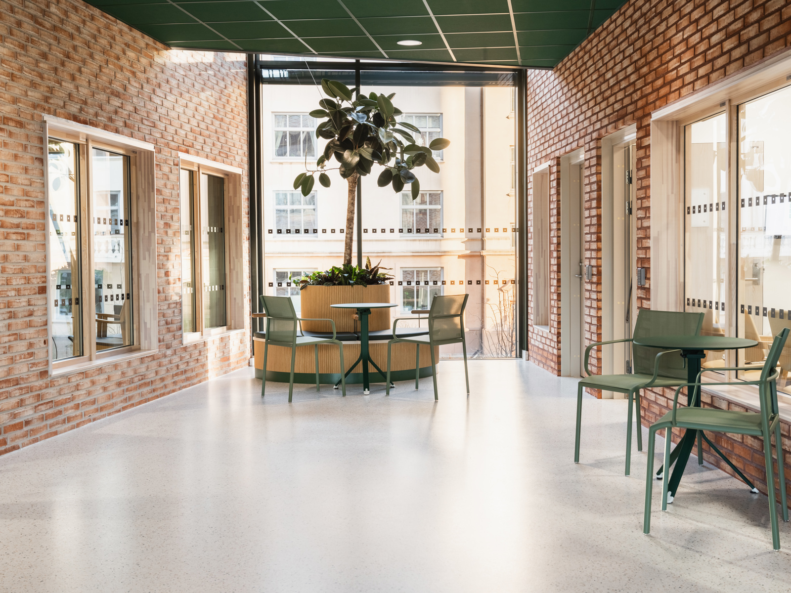 Interiørfoto av gangareal i Majorstuhjemmet, med sittegruppe, plantekasse, eksponert tegl og større glassflate.