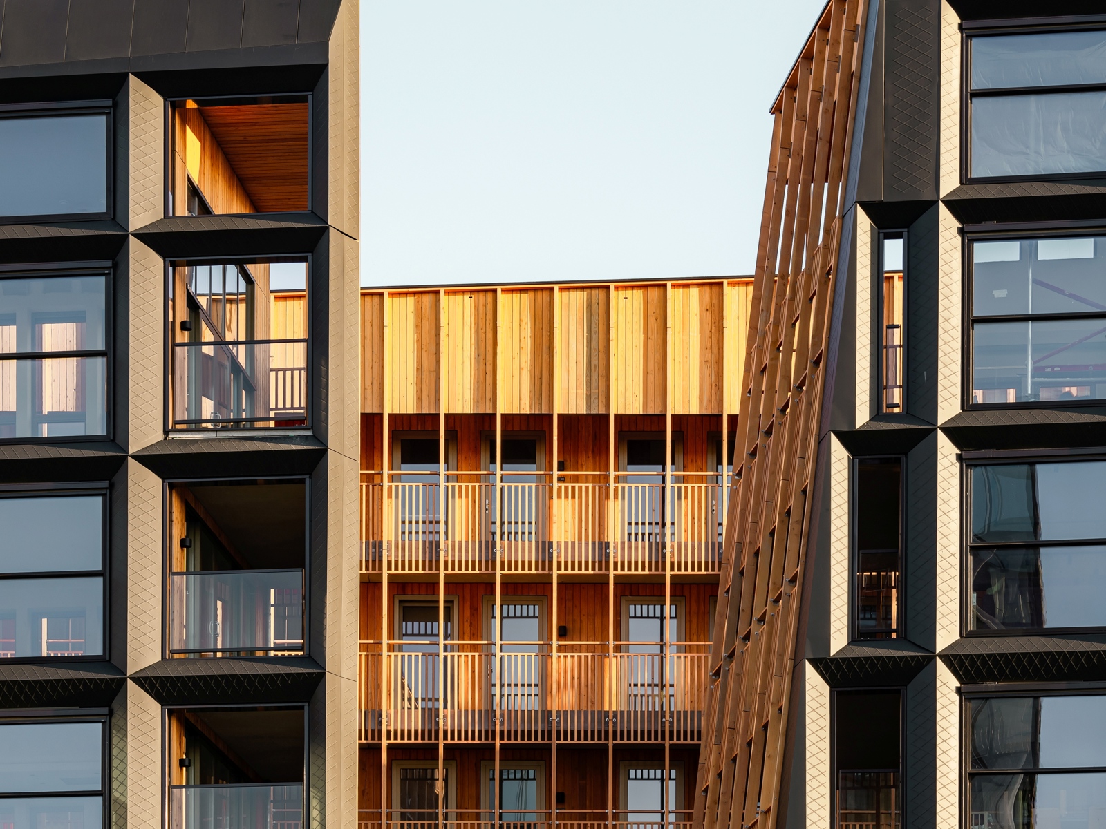Foto av fasade på boligprosjekt, metallfasade med en varm trefasade innenfor. 