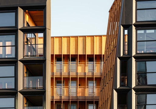 Foto av fasade på boligprosjekt, metallfasade med en varm trefasade innenfor. 