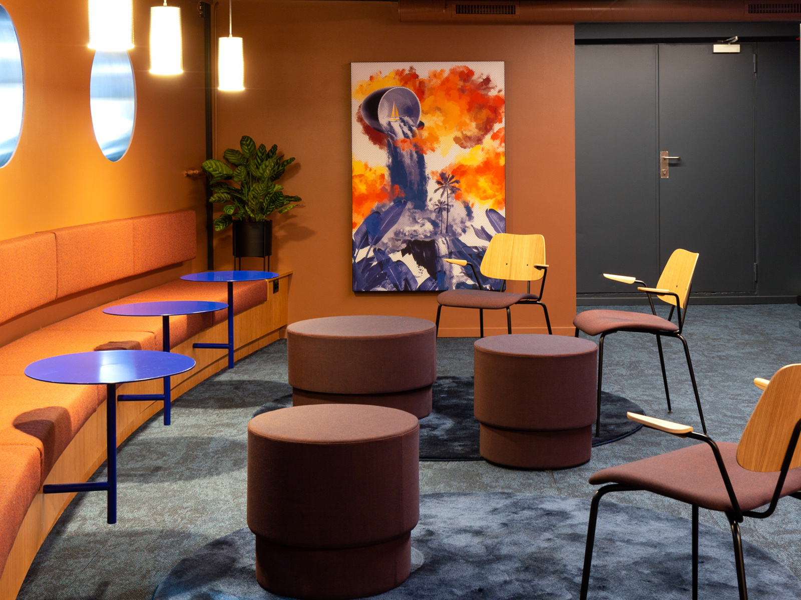Interiør i oransje, blå og lilla toner. Sittegrupper, stoler og benk langs veggen. Foto.