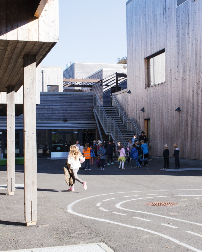 Uteområde på skole, eksteriør. Barn som løper. Foto.