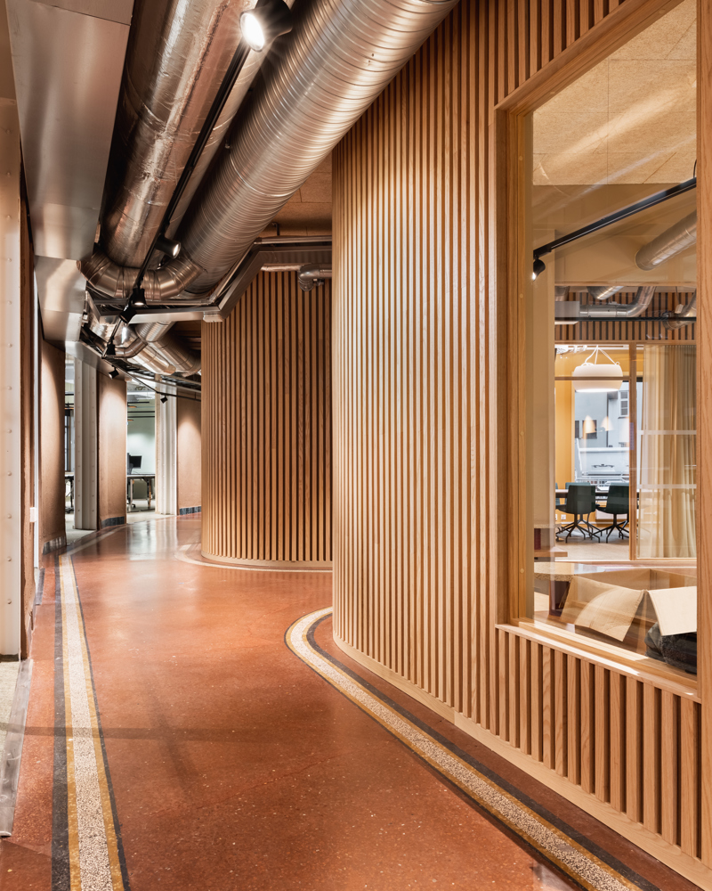 Interiørfoto av en gang med rødt gulv, kurvede spilevegg og synlig ventilasjon i taket.