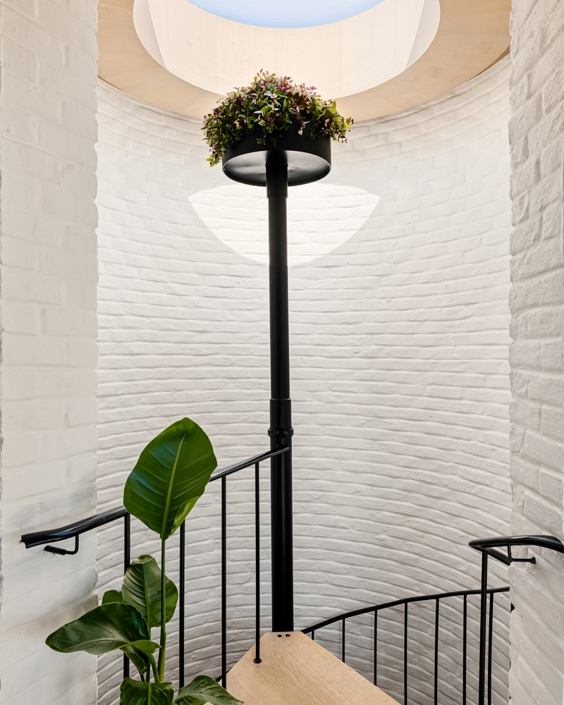 Interiør foto av sirkeltrapp med rundt takvindu som slipper inn lys og svart midtstolpe.