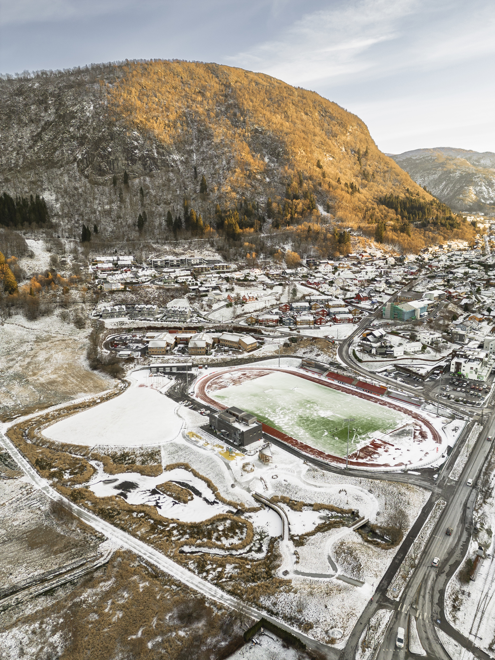 Drone/Fly-foto av delvis snødekt bygd med idrettsanlegg.