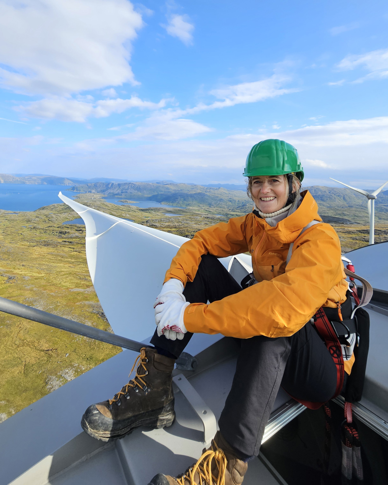 Fotografi over intervjuobjektet som sitter på en turbin i Dønnesfjord vindkraftverk med utsikt over naturen i bakgrunnen