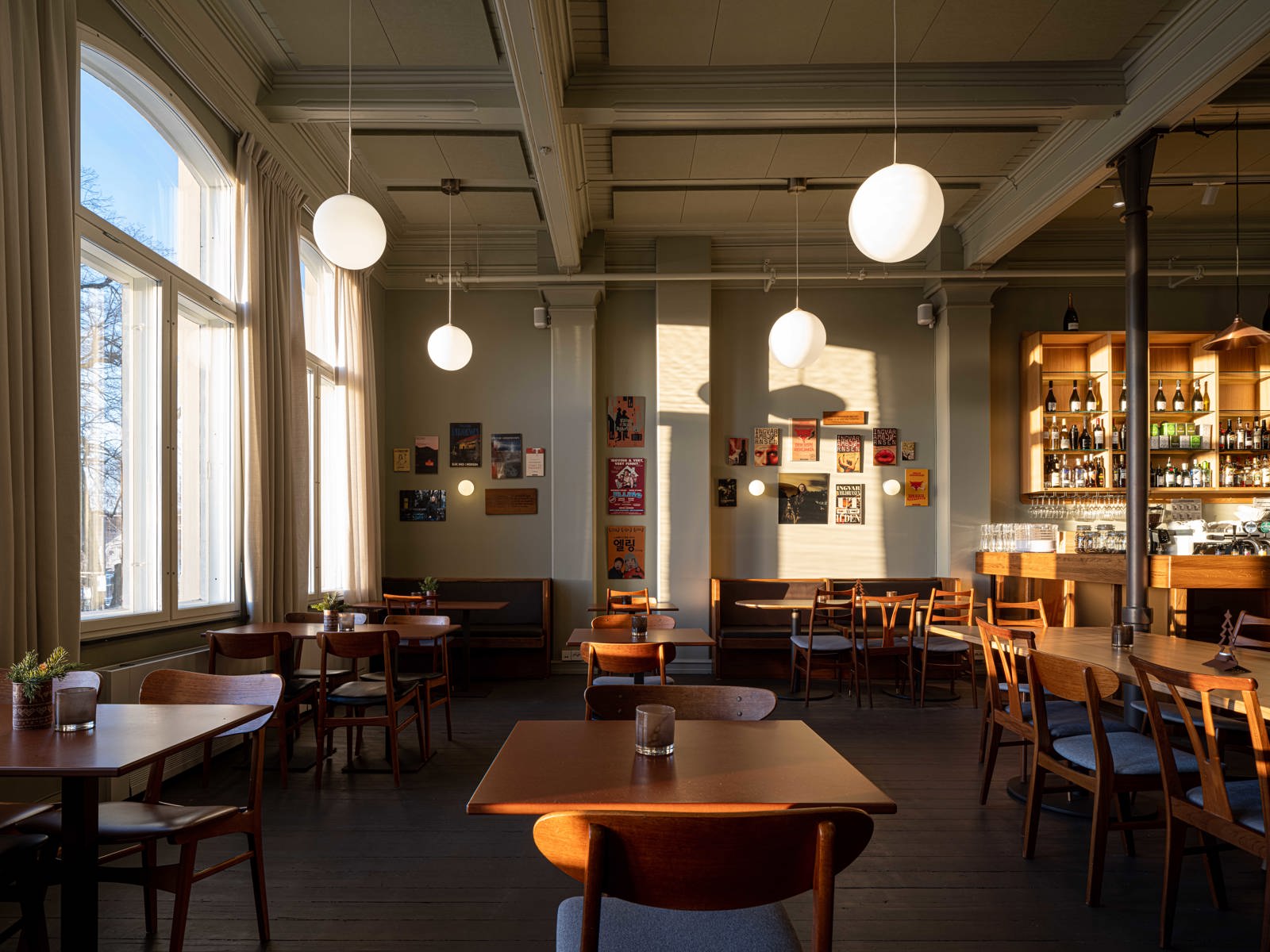 Interiør foto av Ellings kafe, flere sittegrupper, høyt under taket, store vinduer og møbler i varme farger. 