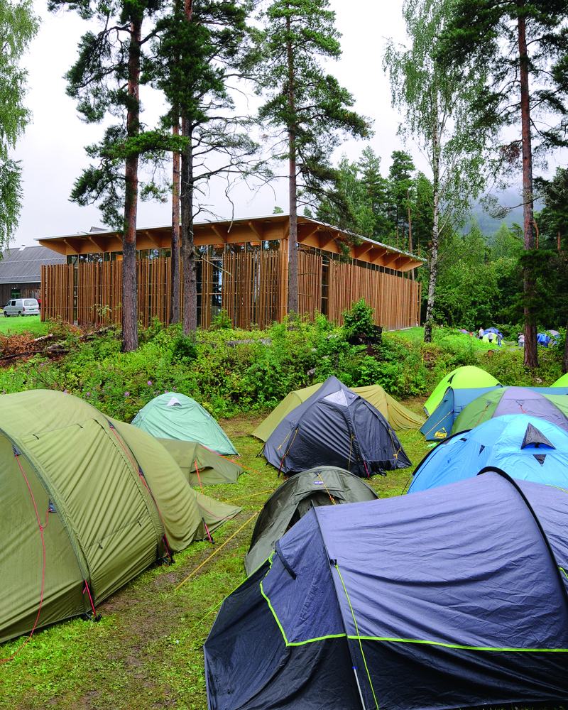 Hus mellom trær i bakgrunnen, flere telt i forgrunnen. Foto