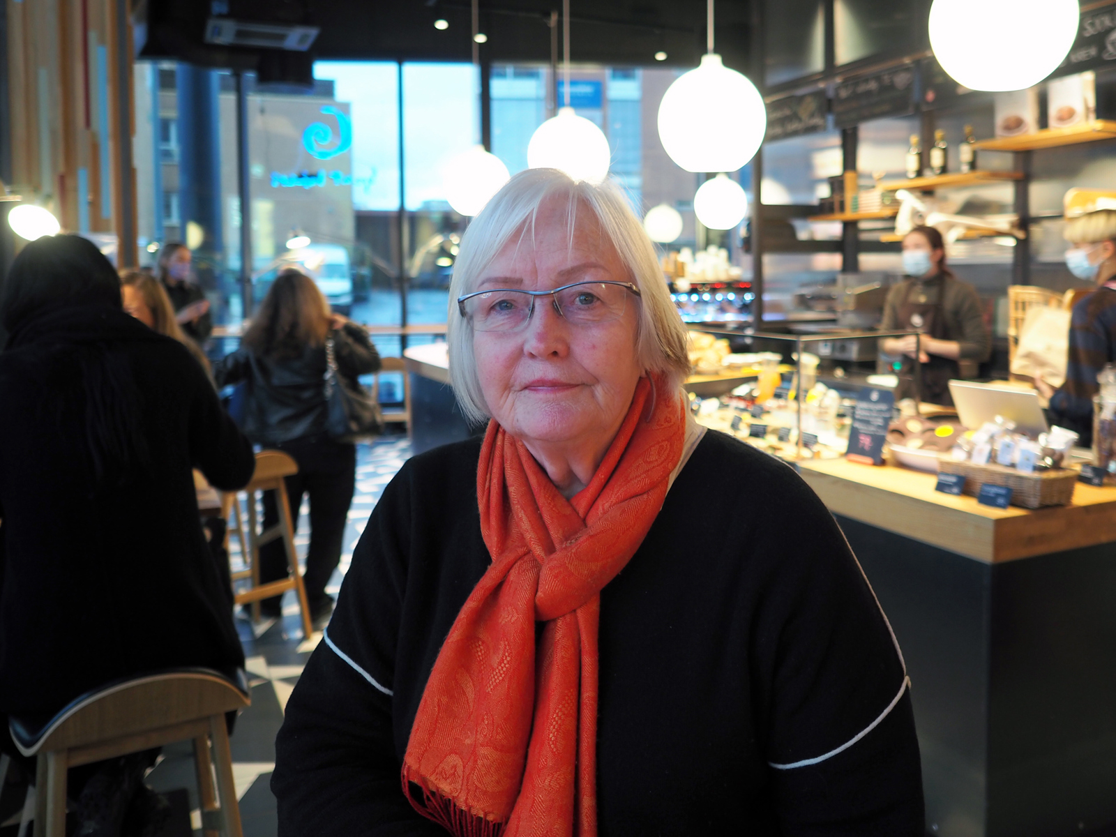 Portrettbilde av Ellen de Vibe inne på en kafe med oransje skjerf. Foto.