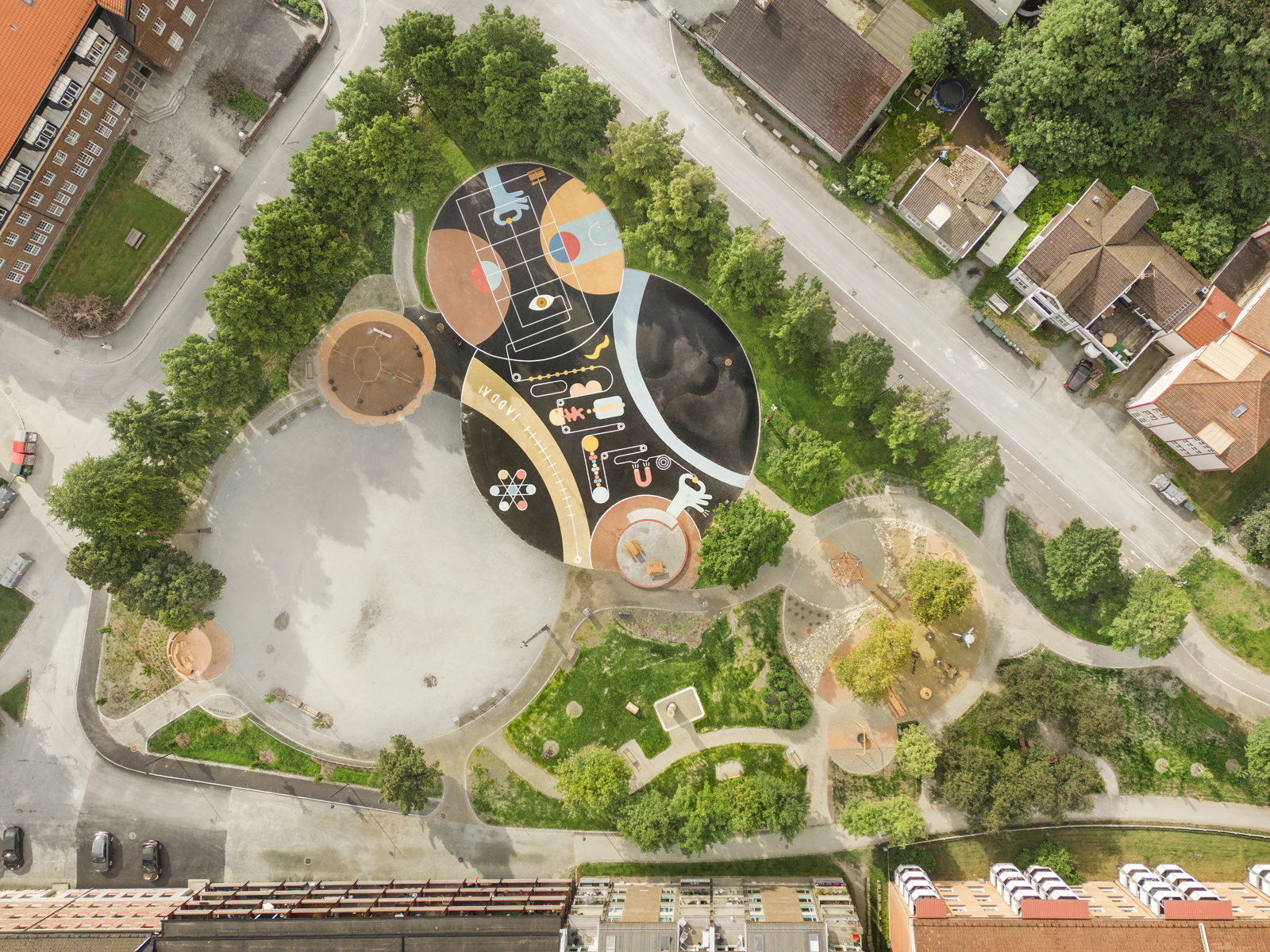 Drone foto som ser rett ned på Buranbanen aktivitetspark, mange ulike materialiteter på bakken, ulike soner og hus som omslutter parken.