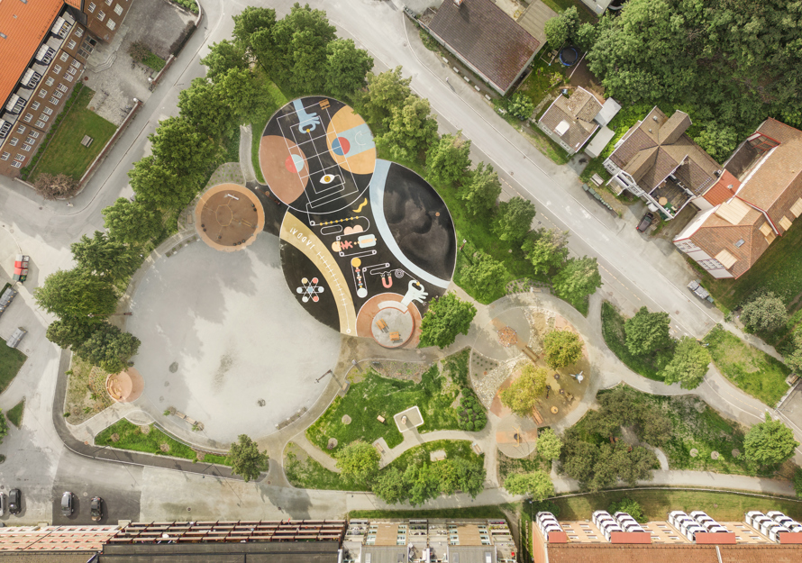 Drone foto som ser rett ned på Buranbanen aktivitetspark, mange ulike materialiteter på bakken, ulike soner og hus som omslutter parken.