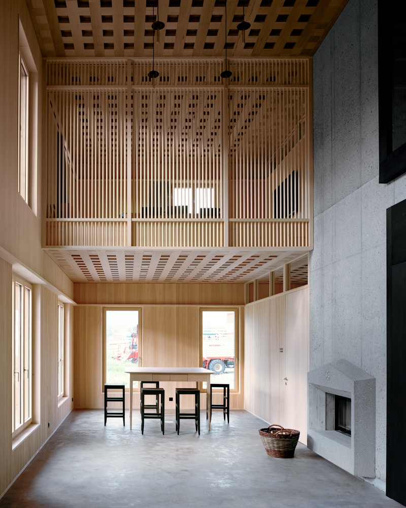 Interiør foto av dobbelt høyt rom i treverk og betong. Sittegruppe og peis. 