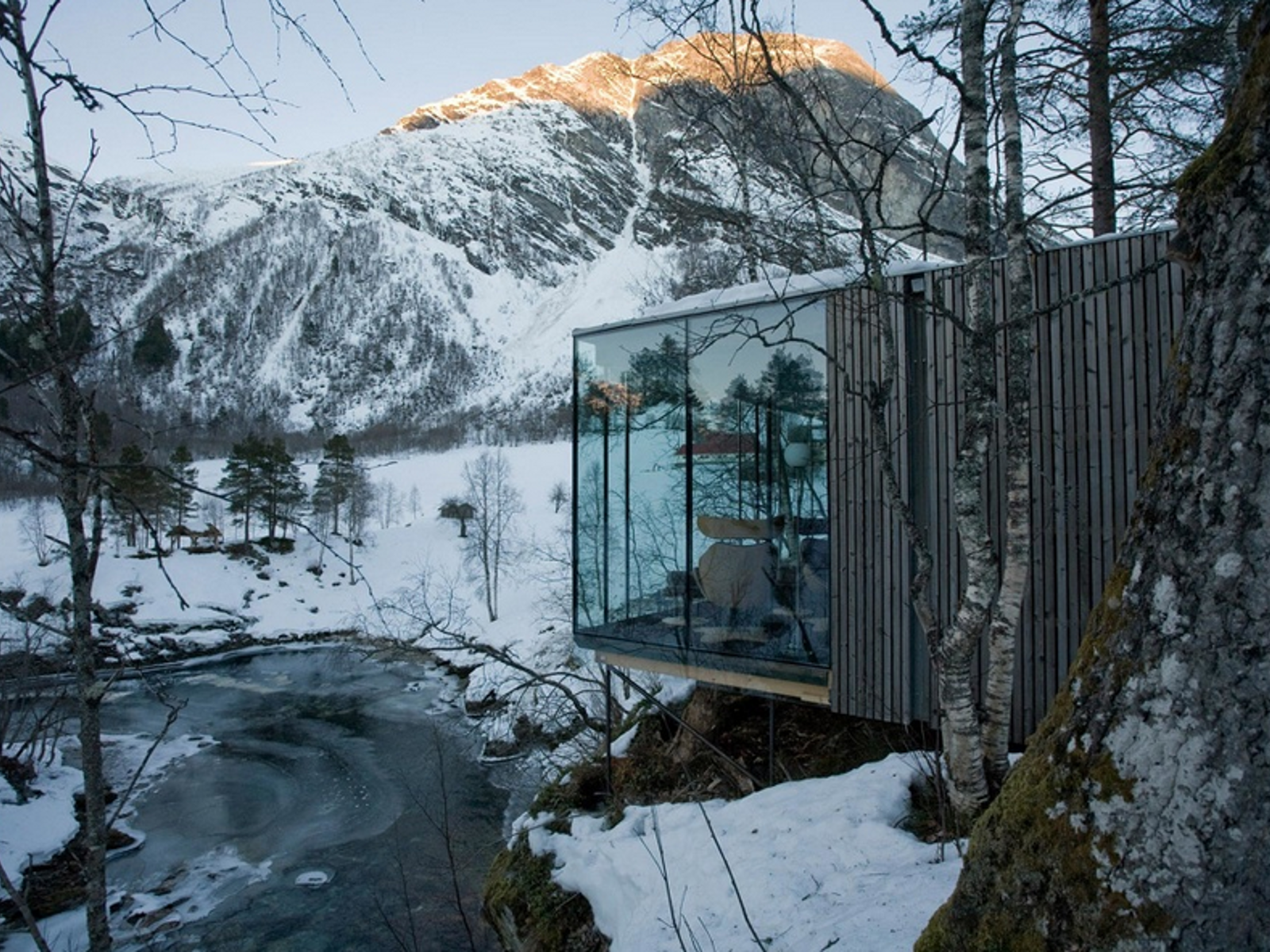 Hytte som kneiser ut i en skråning foran fjell i bakgrunnen