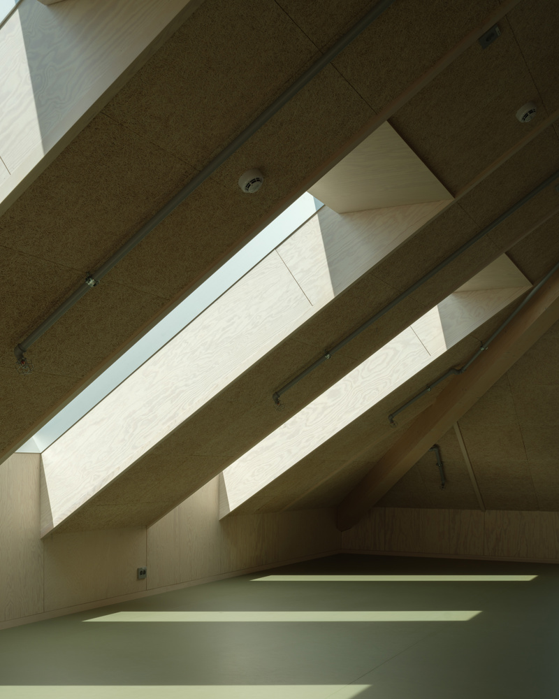 Interiør foto av loftsetasje med store takvinduer i skråtaket, kryssfiner og grønt gulv.