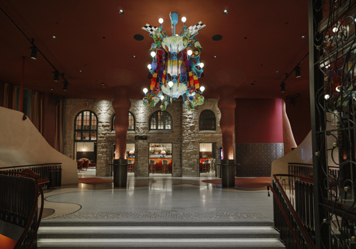 Foto av inngangshall i nye hjorten teater, fargerik lysekrone og røde roner på vegger.