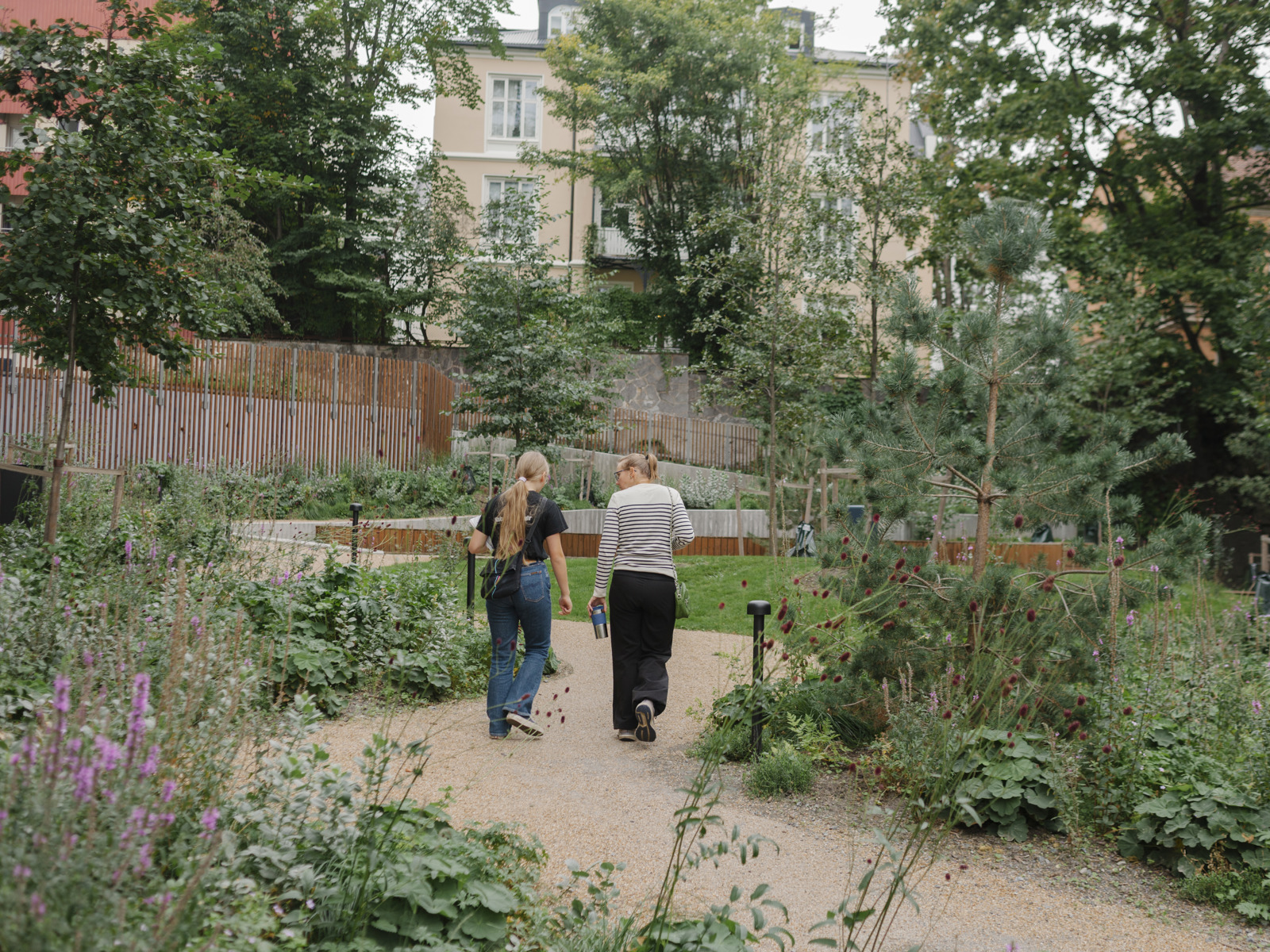 Foto av to kvinner som går på en grussti mellom mye grønn vegetasjon.