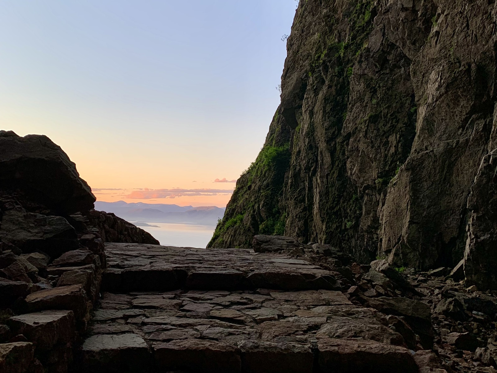 Foto av steinlagt sti, fjellside på høyre side og utsikt over hav og himmel rett frem
