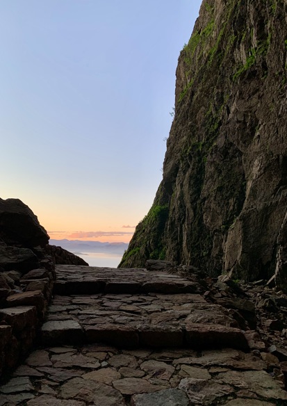 Foto av steinlagt sti, fjellside på høyre side og utsikt over hav og himmel rett frem