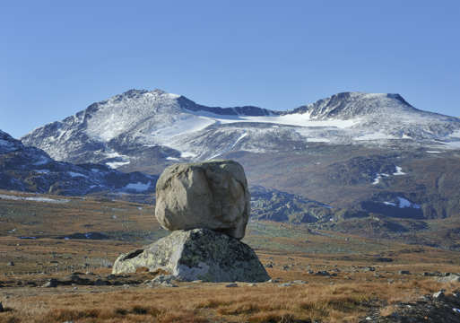 En stein på toppen av en annen stein på høyfjellet, fjell med litt snø på i bakgrunnen. Foto.