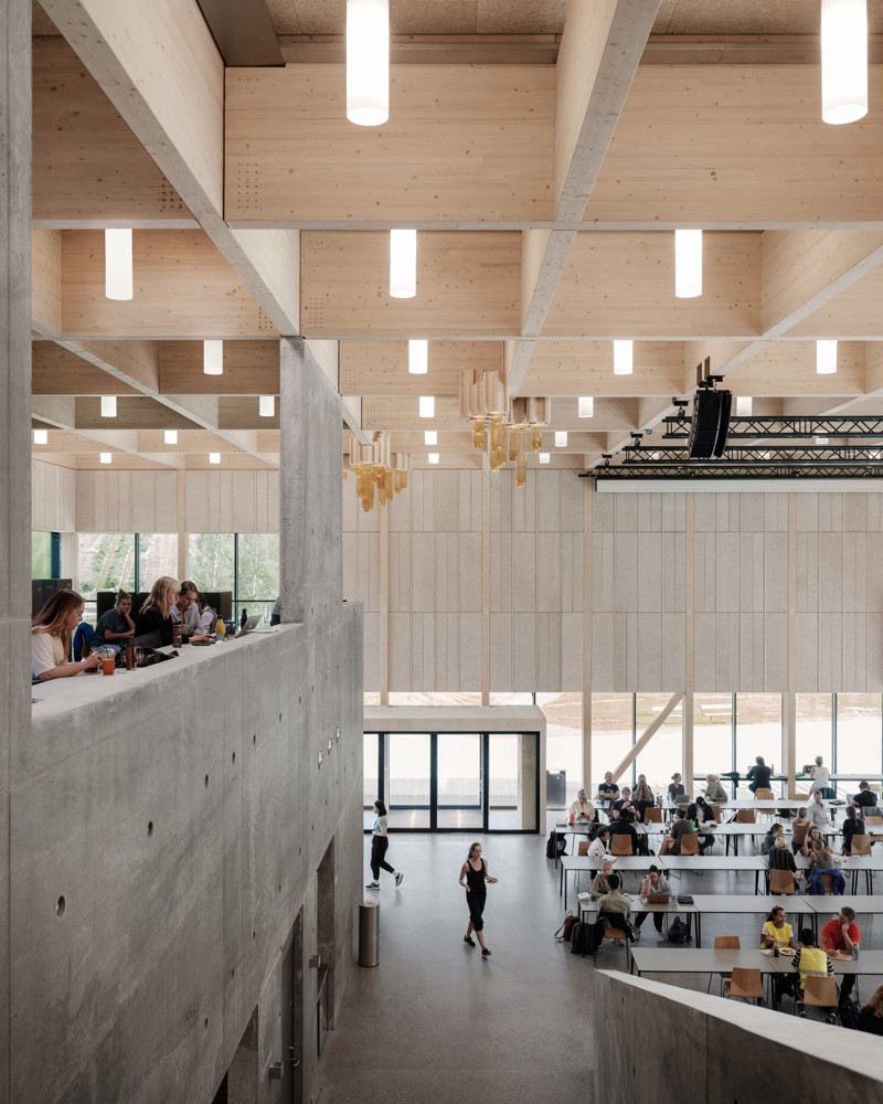 Interiør foto av fellesbygg hos NMBU i ÅS, mennesker som sitter rundt omkring. Betong og trevirke som konstruksjon.