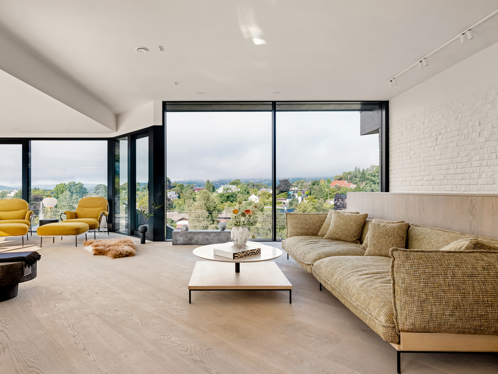 Interiør foto av stue med store glassflater i alle vegger, sofa, lenestoler i gult.