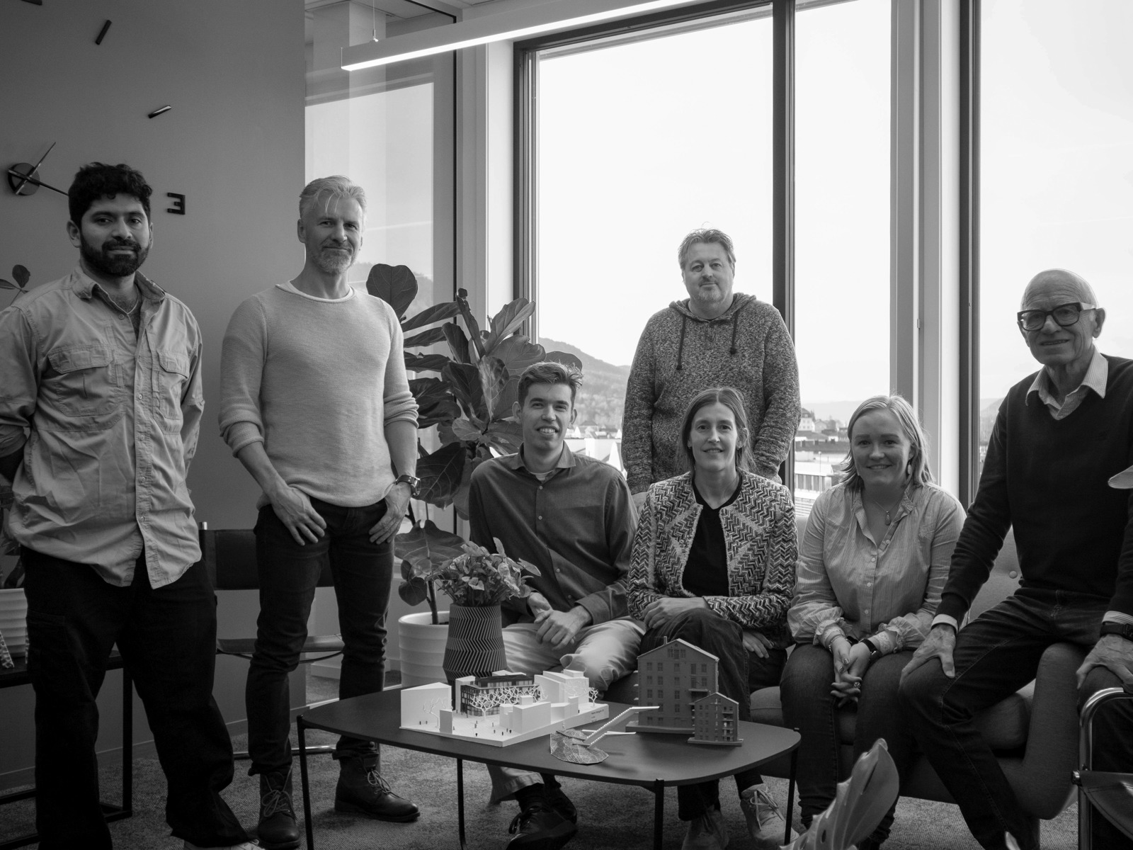 Gruppefoto av et arkitektkontor sittende og stående på kontoret sitt.