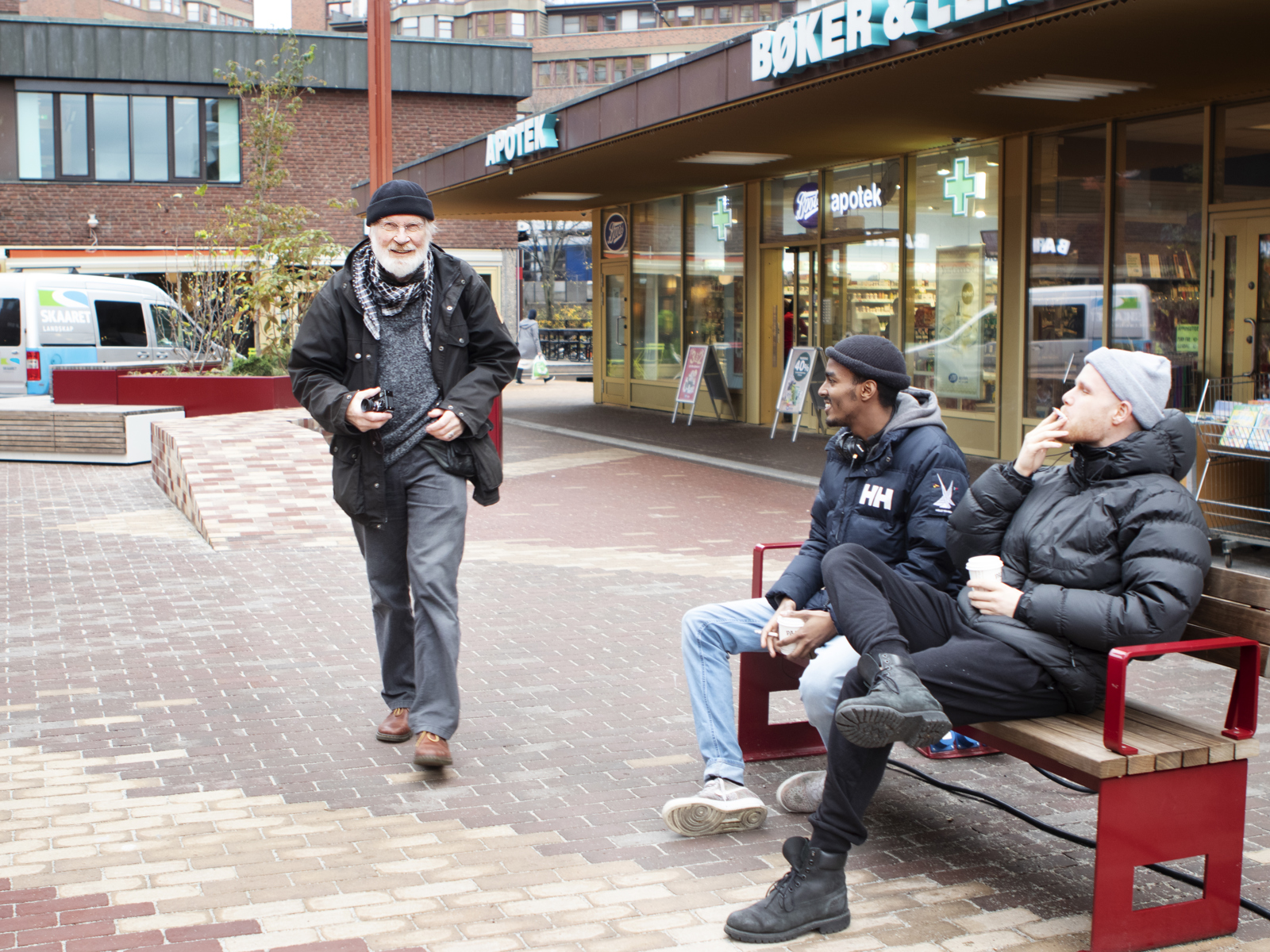 Mennesker sitter og går på torgplassen. Foto.