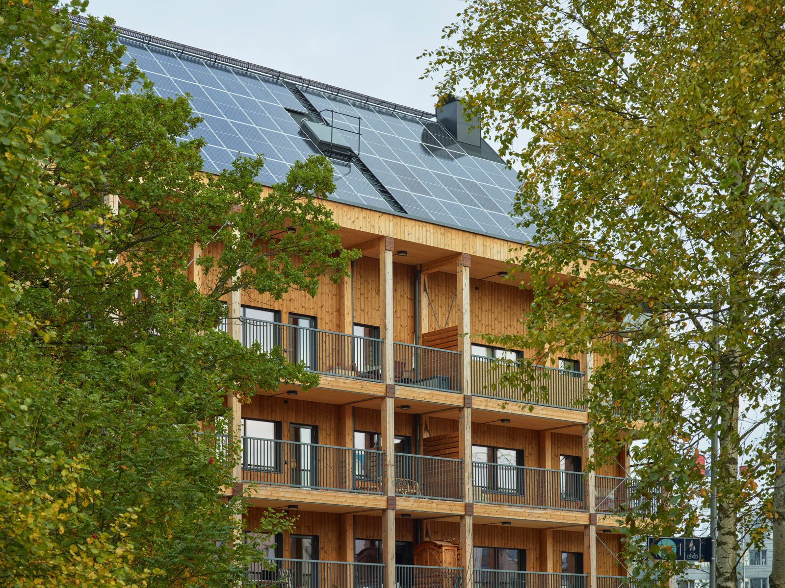 Foto av leilighetsbygg i treverk, trær i forgrunnen.