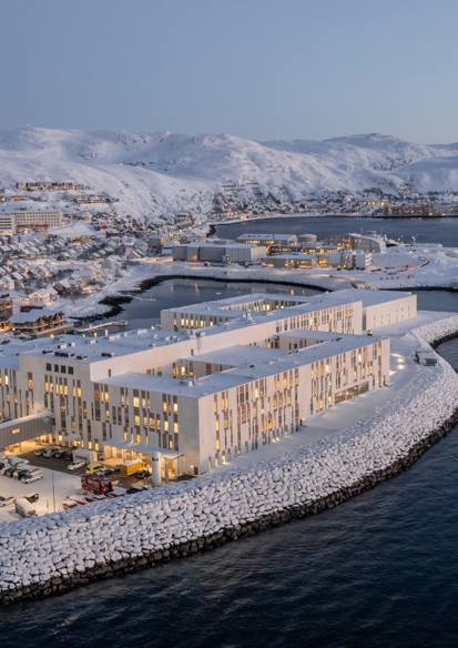 Oversiktsfoto av Hammerfest sykehus på havnekanten. Vinterlandskap med hav rundt.