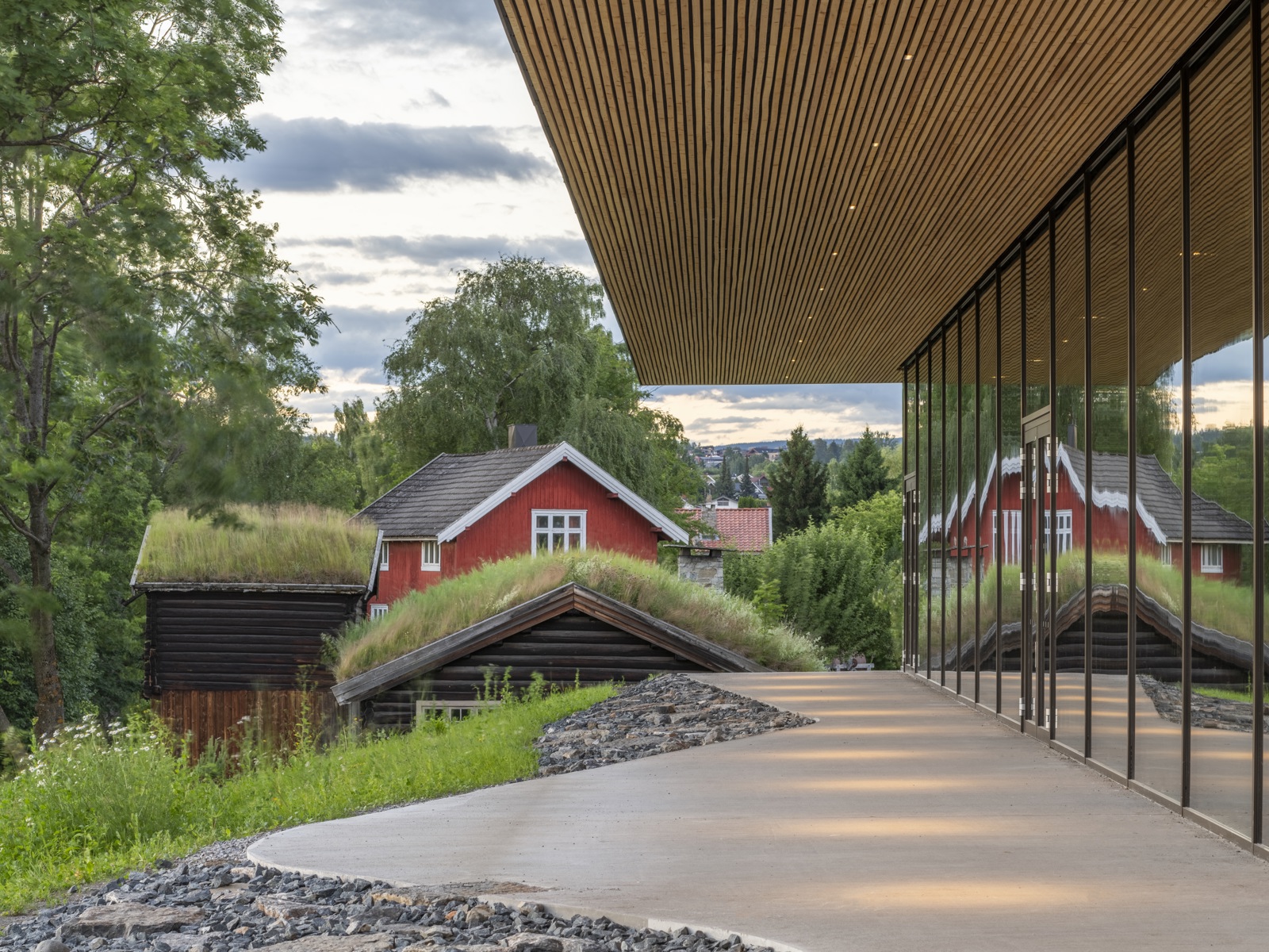 Eksteriørfoto som viser byggets fasade og overheng på taket. Fjøs sees i bakgrunnen.