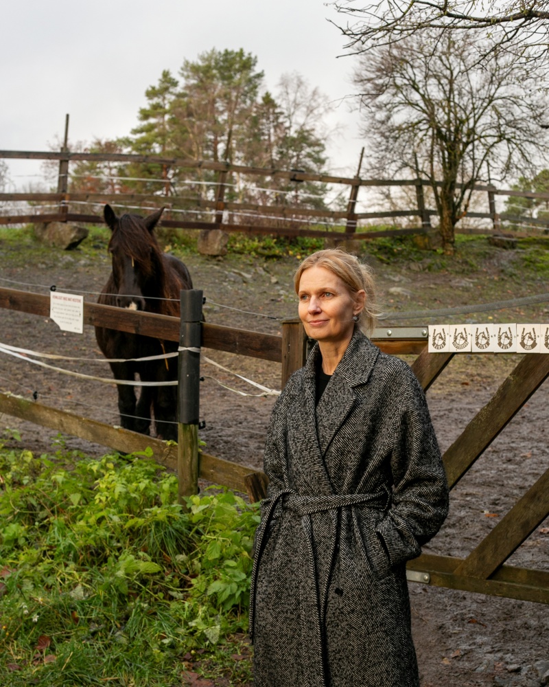Foto av Kristin Lie Romm som står fremfor en innhegning med en hest i.