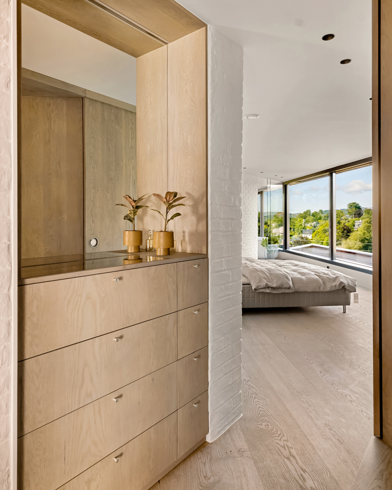 Interiør foto av soverom, kommode med speil i front, seng med store vinduer fremfor i bakgrunnen.