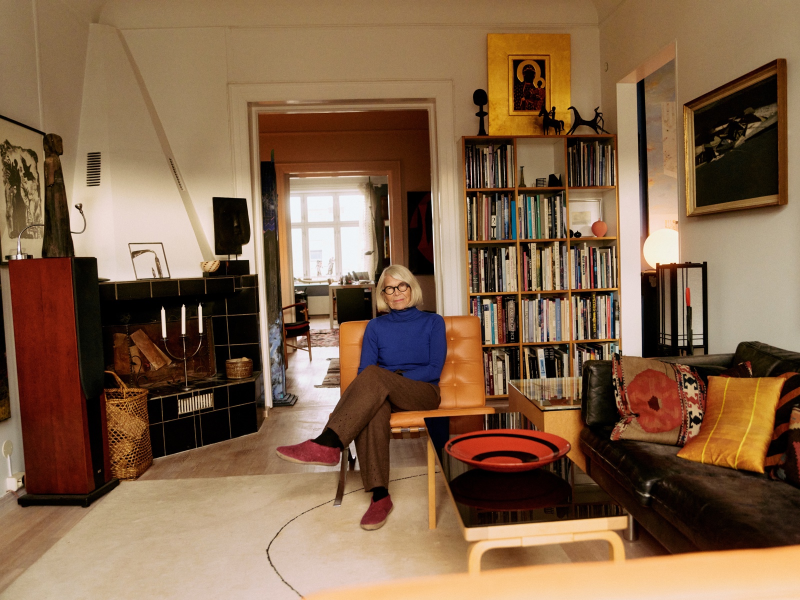 Foto av en eldre kvinne i blå genser som sitter på en stol i stuen sin.