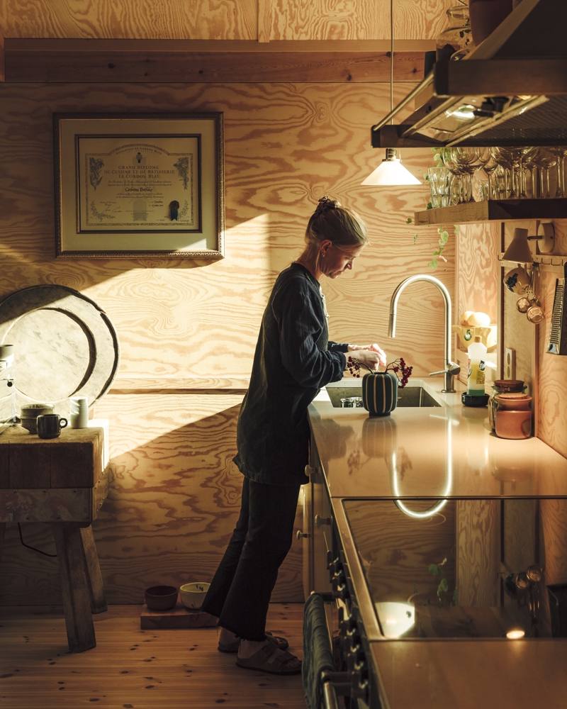 Interiør foto av kjøkken i treverk, kvinne vasker opp.