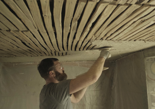 Foto av en mann som påfører kalkpuss på et tak innvendig.