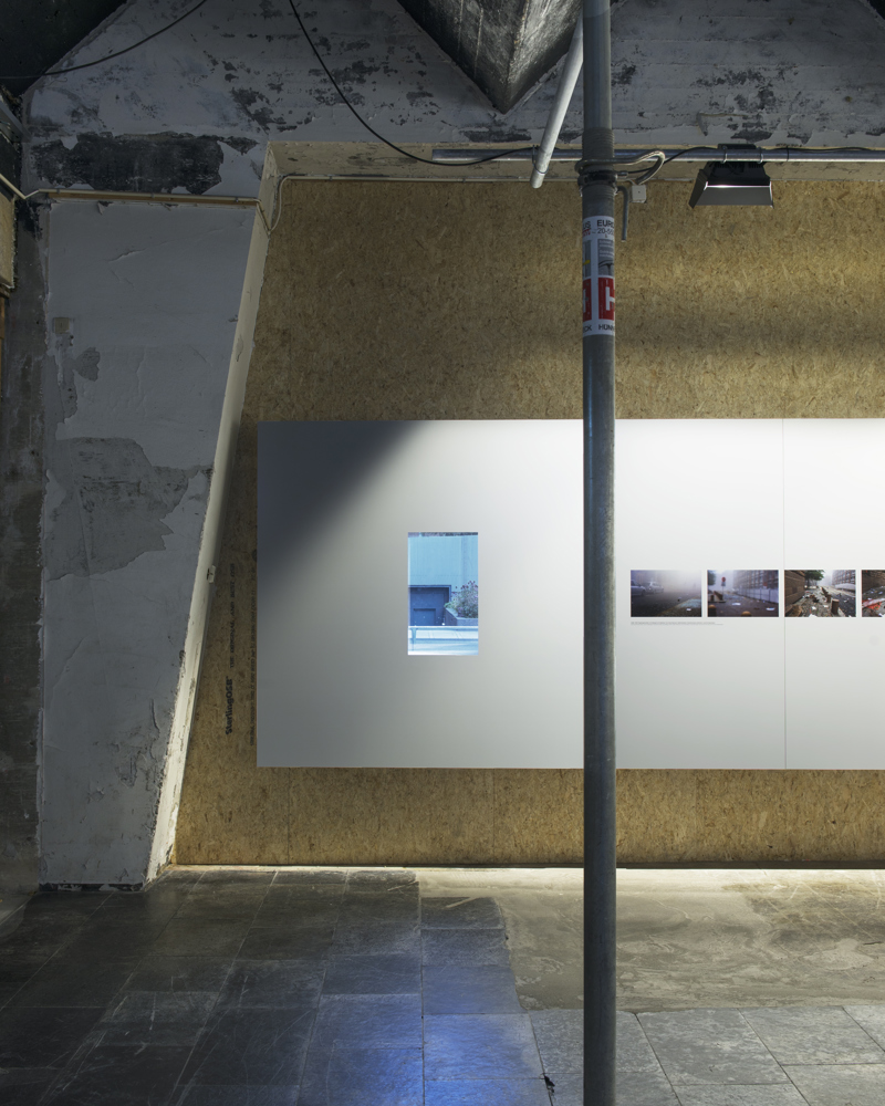 Interiør, slitte vegger, med hvit utstillings vegg med bilder. Foto.